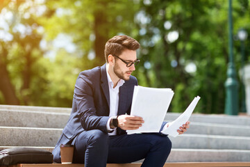 Corporate employee working with business papers on stone stairs in city park