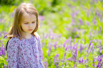 small sad girl alone in field of purple flowers. child is unwell because of heat