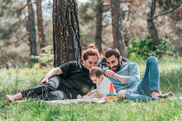 Happy young family with small 8 month daughter having picnic in forest. Cute, Happy, Funny family concept. Father and Mother are playing with daughter and smiling.