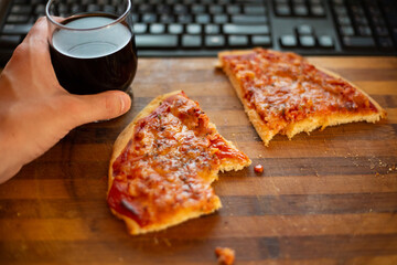 Couple of slices of pizza and glass of drink in man's hand, on old wooden cutting board, in front...