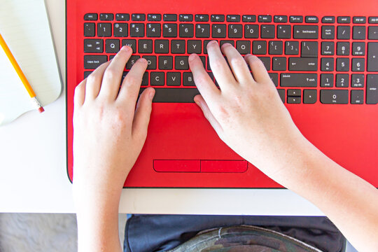 Boy typing on the keyboard of a red laptop during online learning from home