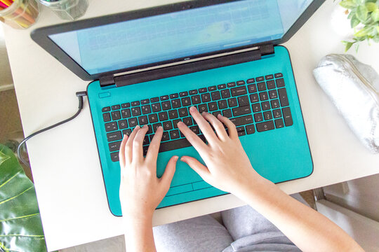 Girl using teal laptop for online learning at home.