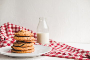 a glass milk bottle with a stack of homemade chocolate chip cookies and red and white tablecloth on a white background. Healthy wholesome homemade treat. gluten and dairy free