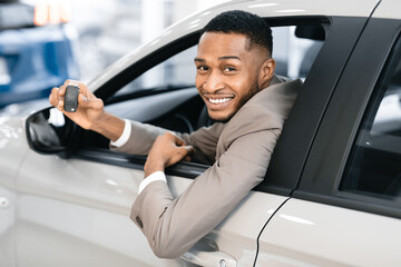 Businessman Showing Key Looking Out Of Auto Window In Dealership