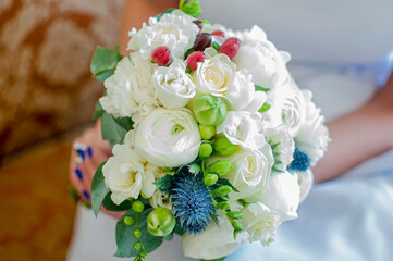 a wedding bouquet of white roses with blue, green and red flowers in the bride’s hands.