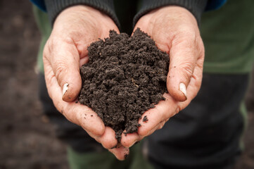 Farmer's hands hold a pile of fertile land in the field.