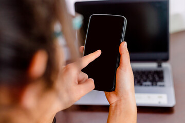 a girl with a black phone in her hands sit in front a laptop