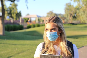 A portrait of a student wearing a face mask and holding a textbook.