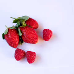 three large ripe strawberries and raspberries lie on a white background