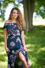 Fototapeta premium Gorgeous young Caucasian woman in blue off the shoulder dress posing in a small cleaning, holding up skirt slightly