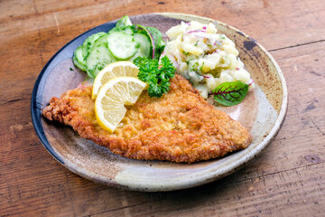 Traditional deep fried veal steak with potato and cucumber salad offered as closeup on a rustic plate with copy space