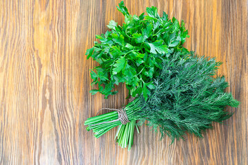 Two bunches of green parsley and dill on brown textured wooden background. Horizontal with copy space. Fresh spices from garden, Healthy greens full of vitamins. Vegan ingredient. Top view
