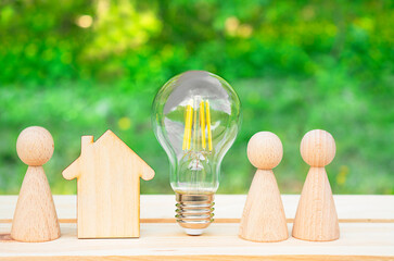 Family concept. Wooden house, lightbulb and many little men on a wooden table. Energy saving, debts...