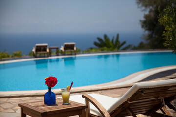 Fresh summer cocktail and sunbed. Swimming pool with mediterranean background.
