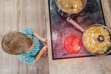 Toddler plays on kitchen with cooker for cooking. Child accident or burn. Unsafe home. Warning for...
