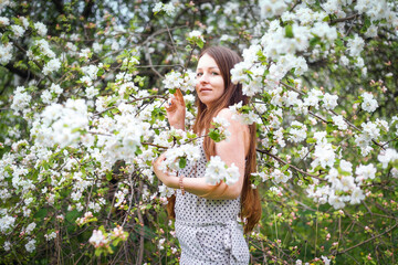 A pretty girl poses in the garden near a blooming Apple tree with white flowers. Spring garden. Beautiful women's hair. Portrait of a beautiful model.