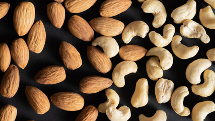 Scattered peeled almond and cashew nuts on black as background, top view. Healthy food. Different healthy nuts