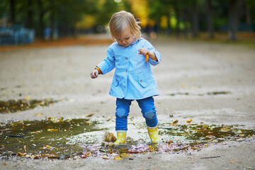 Child wearing yellow rain boots and jumping in puddle on a fall day