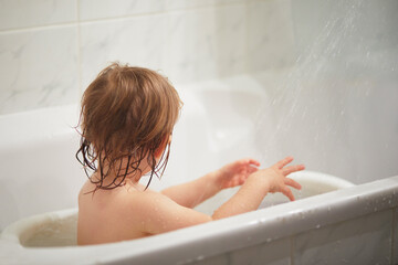 Cute little girl playing with rubber toys in small bathtub.