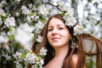 Fototapeta premium Portrait of a beautiful girl with long hair, in an Apple orchard. Spring garden. White flower. An Apple tree blooms in the Park. Model with beautiful hair.