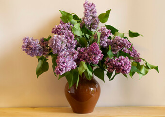 Beautiful bouquet of terry lilacs with green leaves in a brown ceramic vase.