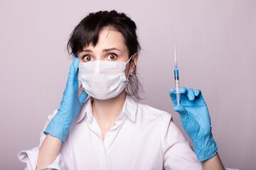 girl in a white shirt, a medical mask and gloves, holds a syringe with blue liquid in her hands