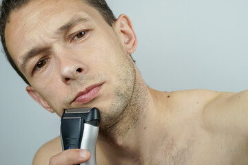 Portrait of a beautiful dark-haired man with an electric razor on a light background. Dark-haired...