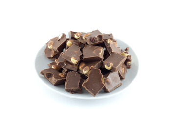 Pieces of milk chocolate with hazelnuts on a saucer isolated on white background