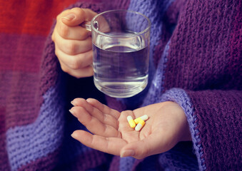 Female hands holding a glass of water and pills