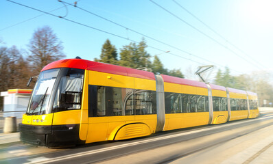 Naklejka na ściany i meble Modern urban rail transport. Yellow tram with motion blur effect moves fast in the city. High speed passenger train in motion on railroad.