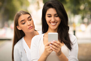 Envious Girl Peeking At Girlfriend's Phone While She Texting Outdoors