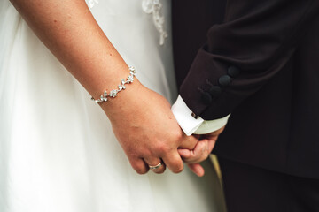 Wedding couple standing and holding hands. Closeup bride's jewelry bracelet on wrist. Wedding day concept.