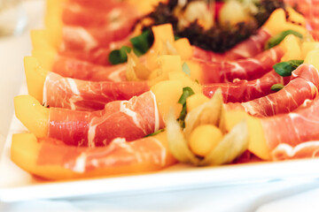Closeup of tray with juicy slices of yellow melon rolled into ham. Self-service buffet table....