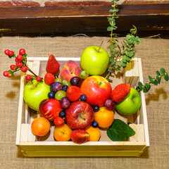 Set of berries and fruits in wooden box. Apple, strawberry, grape, berry and peach on a red brick...