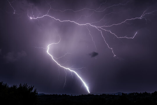 Two dramatic lightnings discharging over the ground and purple sky on at night in Romania over rural area
