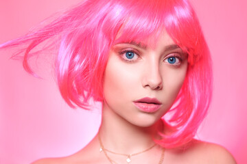 Fototapeta premium A girl in a pink wig, on a pink background fashion, pink makeup, a serious face, the model is pooping. Bright photo portrait of a girl with blue eyes