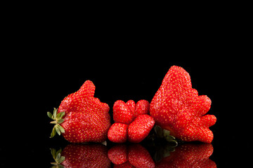 Ugly berries of organic strawberries on a dark background with reflection. Trendy food. Copy space