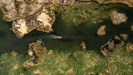 Aerial top-down view on motor speed boat rushing through pathways created by totora plant on the way to Uros floating islands at Lake Titicaca close to Puno, Peru; abstractive texture and patterns.