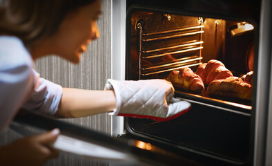 Happy woman removing hot croissants from oven at home