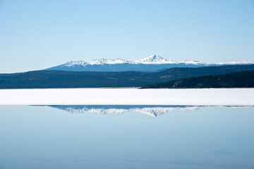 Pristine and calm lake in Yukon Territory with amazing reflection on blue sky day with snow capped mountains in spring time. 