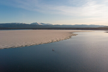 Sunset drone aerial view of person kayaking on blue pristine, stunning lake in northern Canada with ice. 