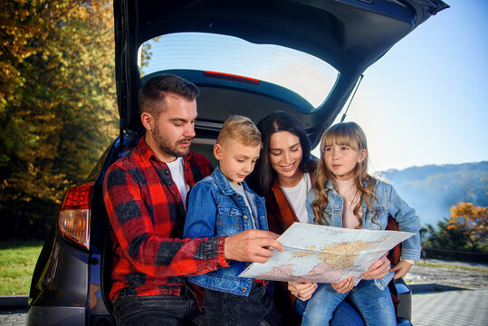 Close up of joyful pleasant family which gethering on their vacation with teen children and using road map to choose the right path on the car