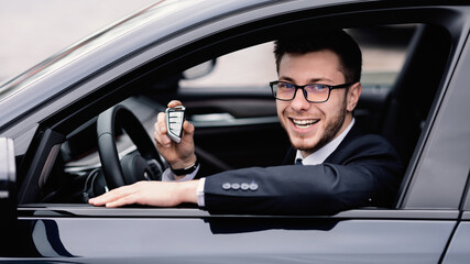 Fototapeta na wymiar Young bearded man showing auto key, sitting on driver's seat