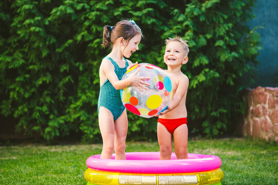 Two Children With Beach Ball At Swimming Pool. Joyful Kid Playing In Inflatable Pool Backyard. Little Kids At Swimming Pool On Sunny Day. Colorful Swimming Pool Ball. Healthy Babies Summer Activity