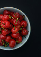 Cherries in a light blue porcelain bowl placed on a black background