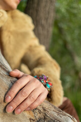 A woman's beautiful hand with a bracelet rests on the trunk of a tree. A bracelet with semi-precious stones. You can see the sleeve of a light fur coat. The nails are not painted. Harmony with nature.