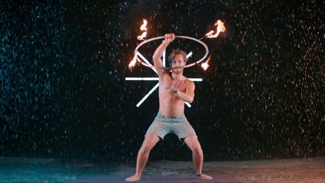Amazing fire dancing performer skills, hula hoop with fire in rain wet studio, super slow motion