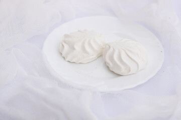 Two white wavy marshmallows zephyr lying on plate on airy snow white cloth