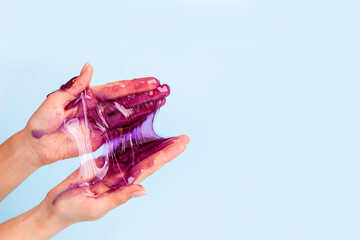 Young girl hands with sticky purple slime on blue background, liquid wax for depilation, conceptual flyer banner with copy space, antistress relax, modern kids hobby oddly satisfying semi surreal asmr
