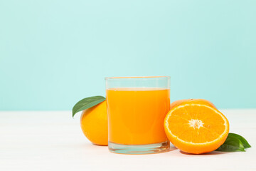 Fresh orange juice in glass and oranges fruit on white wooden table with blue background with copy space.